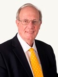 Photograph of Philip R Wood, author of the series. He is an elderly white man wearing a black suit with white shirt and yellow tie. The background is white. 